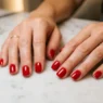 Woman's hands on marble salon table showing perfectly manicured short nails with glossy red polish and professional finish