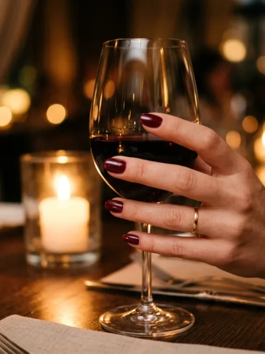 Elegant red manicured hand holding wine glass at romantic candlelit dinner table setting