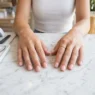 Close-up of freshly applied short squoval acrylic nails in sheer pink resting on a marble nail salon counter