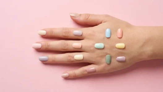 Collage of thirteen simple nail designs in soft pale tones arranged on a pastel pink backdrop under studio lighting
