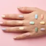 Collage of thirteen simple nail designs in soft pale tones arranged on a pastel pink backdrop under studio lighting