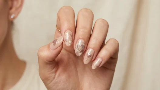 Woman's hand showing sophisticated heart nail art designs in muted earth tones with soft studio lighting