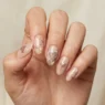 Woman's hand showing sophisticated heart nail art designs in muted earth tones with soft studio lighting