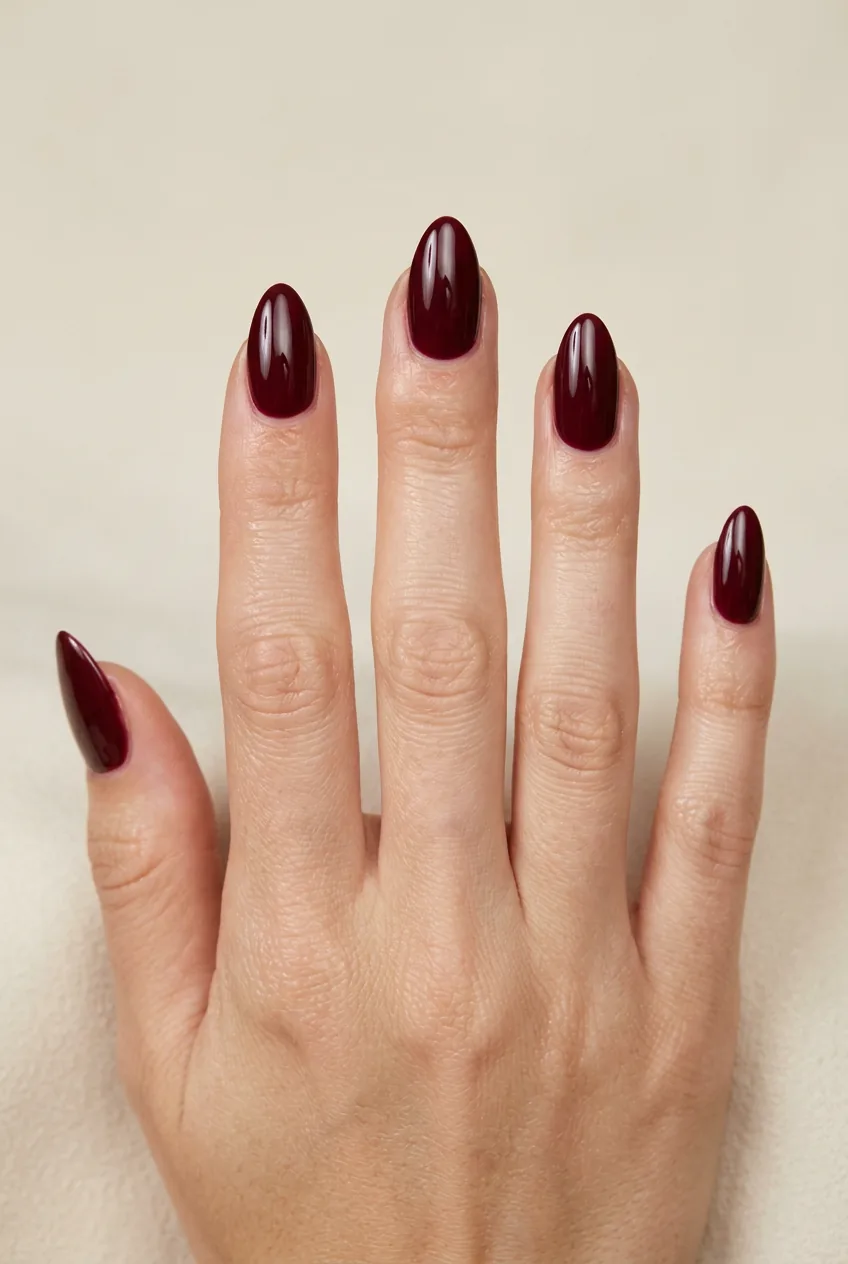 Woman's hand with almond-shaped nails painted in deep burgundy against a neutral cream background