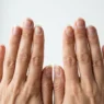 Hands held up at eye level showing long natural nails being assessed before shaping in bright daylight