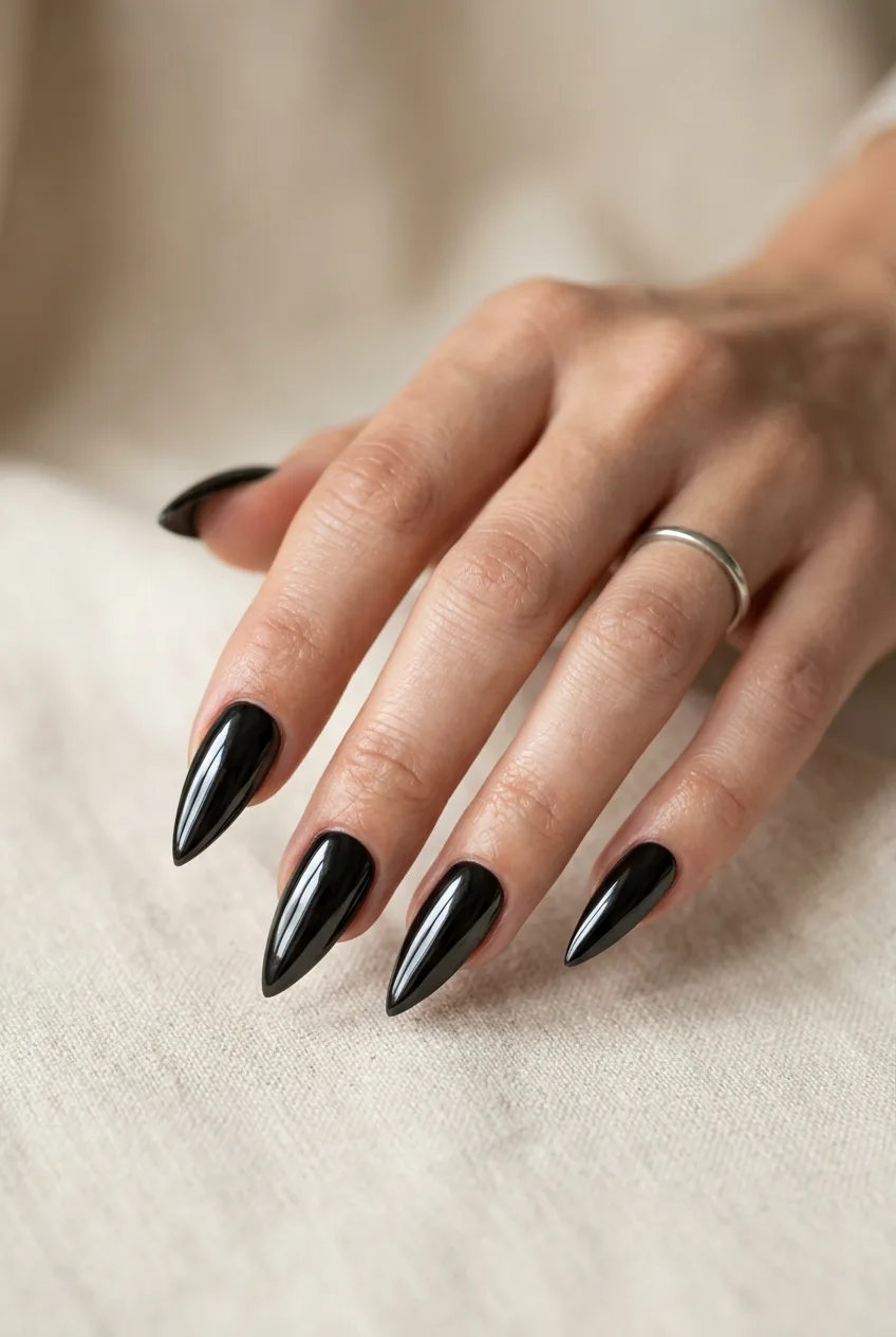 Woman's hand showing long stiletto nails in mirror-finish black chrome catching studio light along each pointed tip