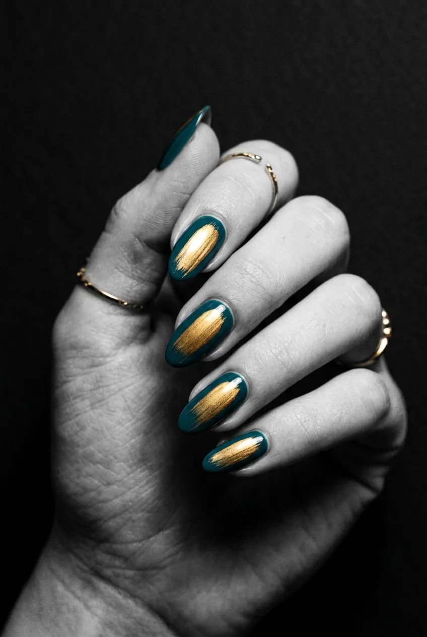 Manicured nails in deep teal with a bold angled gold brushstroke swipe showing confident texture and catching a long highlight under side light