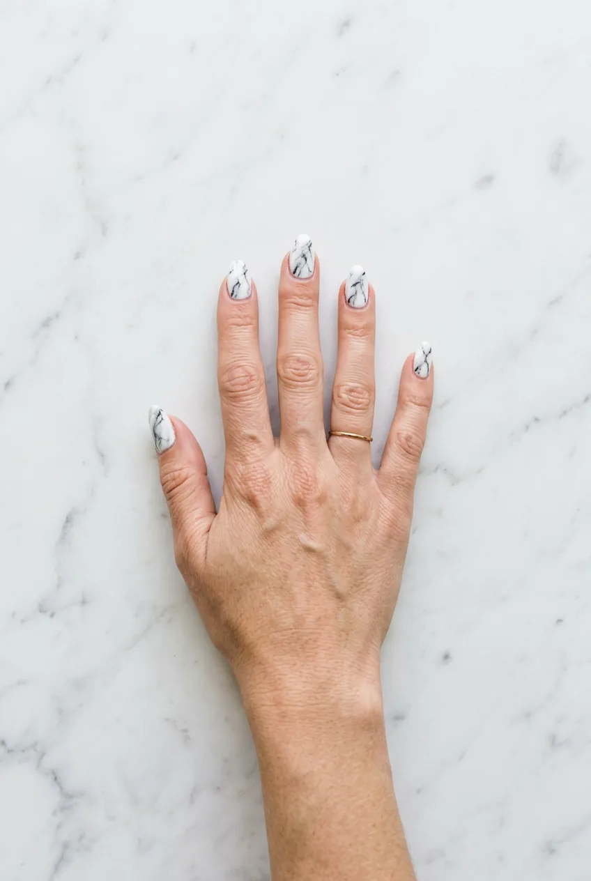 Hand with classic white and grey marble nails in almond shape showing defined charcoal veining in bright daylight