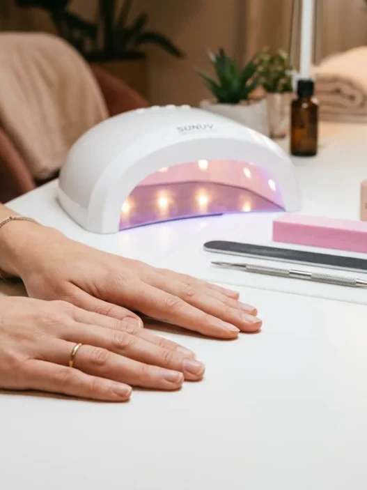Bare hands resting on salon table with nail tools neatly arranged including file buffer cuticle pusher and gel lamp