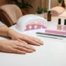 Bare hands resting on salon table with nail tools neatly arranged including file buffer cuticle pusher and gel lamp