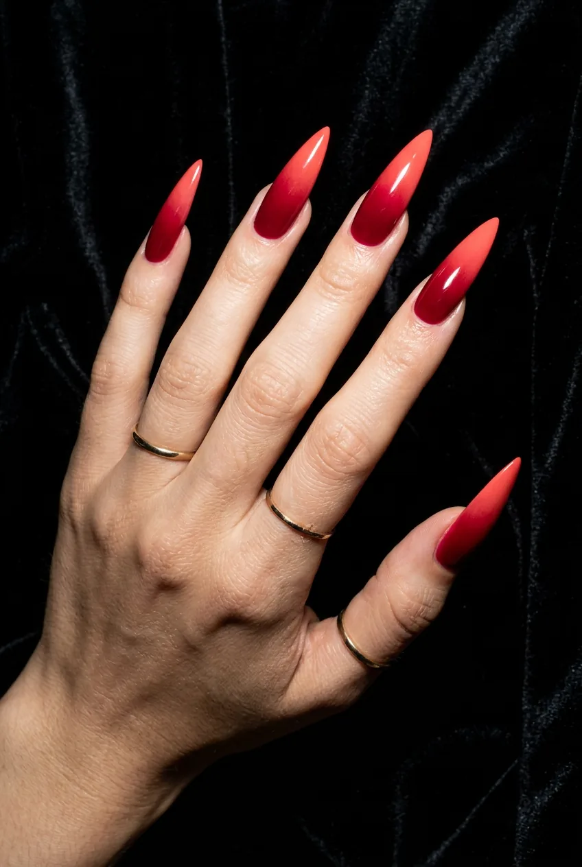 Long stiletto nails in a rich crimson to coral ombre gradient fading from cuticle to pointed tip