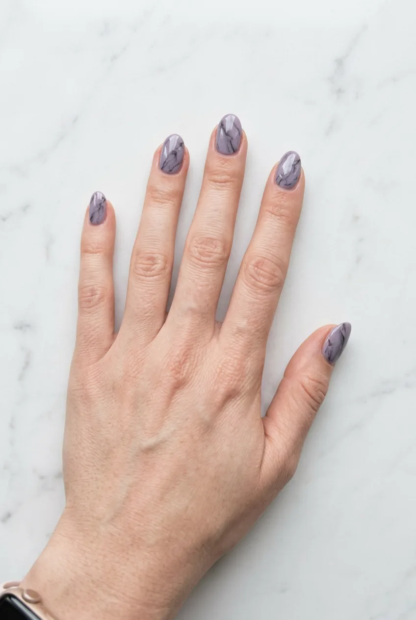 Overhead view of hand with dusty lavender marble oval nails showing soft charcoal veining in cool natural daylight