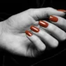 Close-up of manicured nails with a glossy glazed glass finish in warm terracotta against dark velvet background under dramatic side light