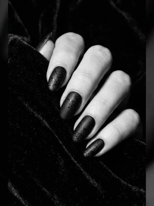 Close-up editorial shot of a manicured hand with deep black Halloween nails against dark velvet background, dramatic side lighting