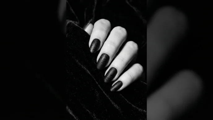 Close-up editorial shot of a manicured hand with deep black Halloween nails against dark velvet background, dramatic side lighting