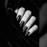 Close-up editorial shot of a manicured hand with deep black Halloween nails against dark velvet background, dramatic side lighting