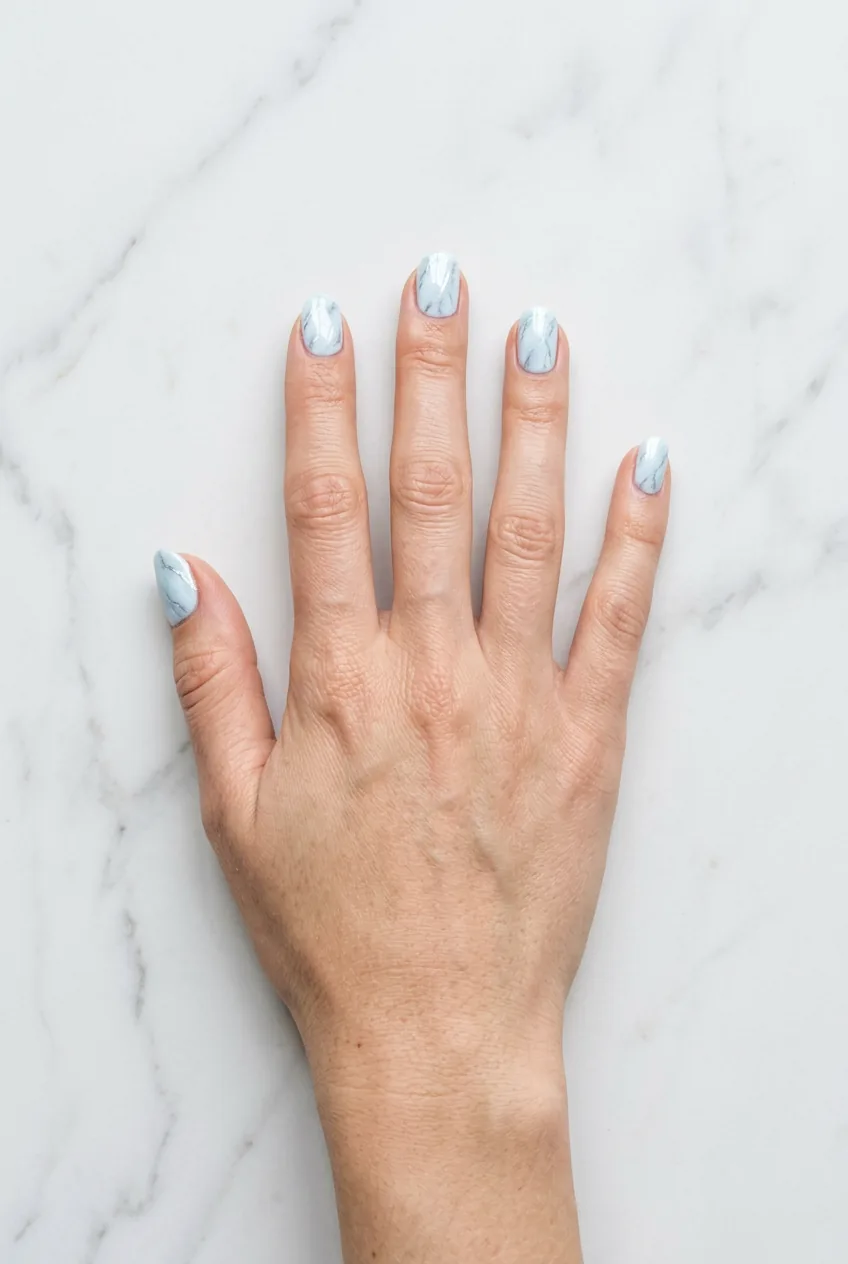 Overhead shot of hand with icy blue marble nails in high-gloss finish creating luminous effect in bright daylight