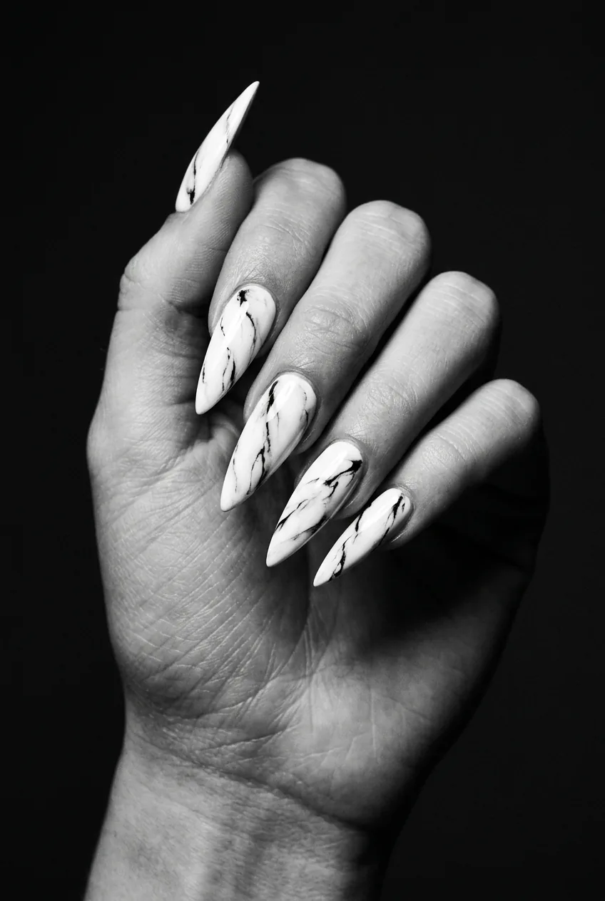 Long stiletto nails showing white marble effect with bold black veining converging toward the pointed tip