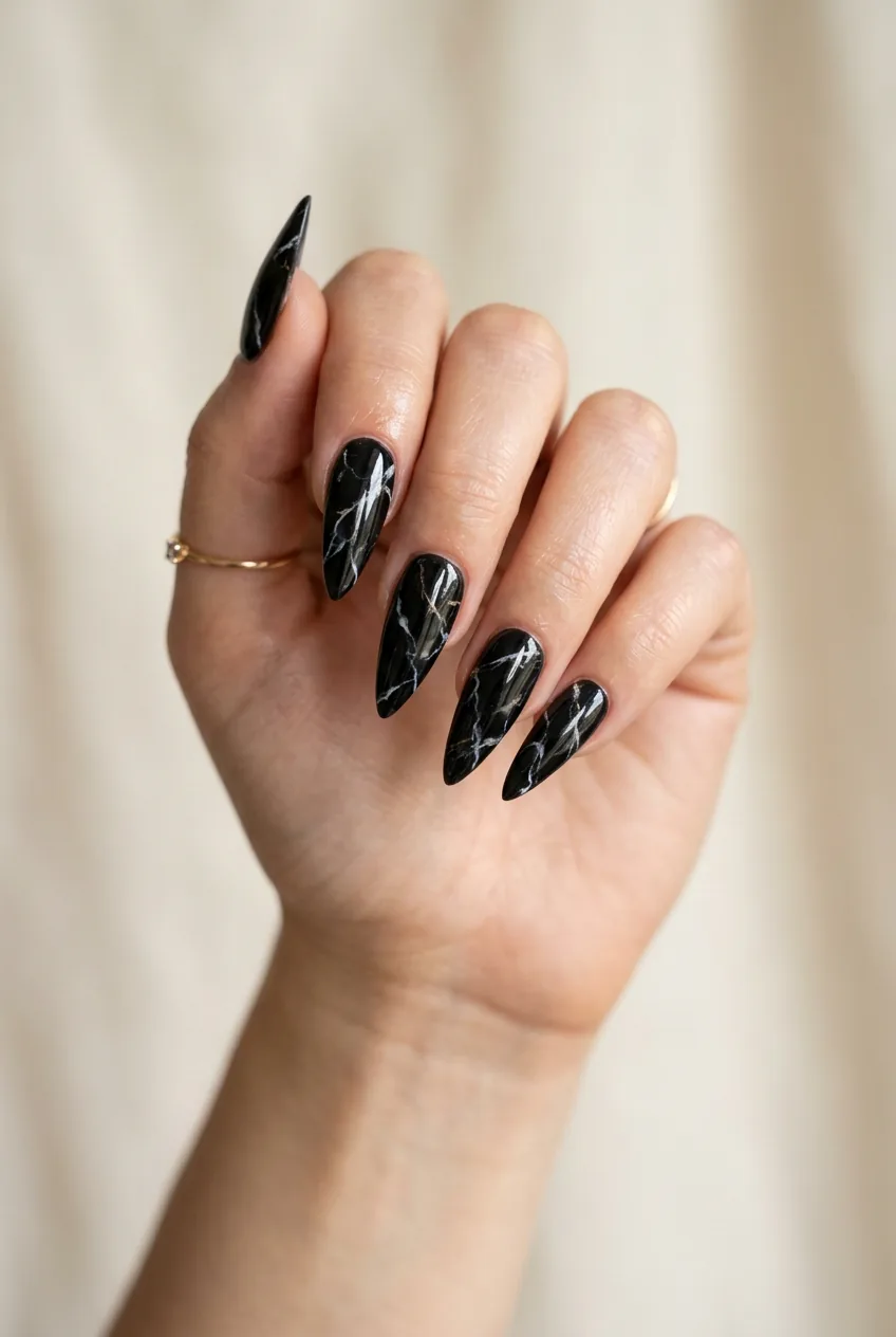 Long stiletto nails with midnight marble black base and delicate white and gold veining under high gloss