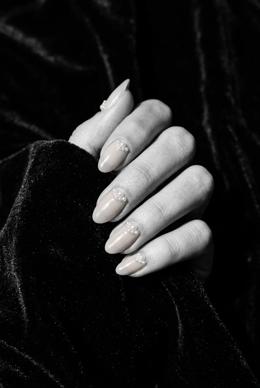 Close-up of nude base nails with tiny pearl bead details near the cuticle catching a sharp precise highlight under editorial side light