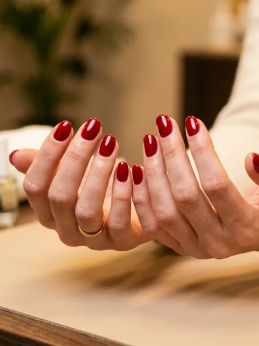 Woman's hands fanned on salon table showing ten freshly finished round nails in classic glossy red gel, warm lighting