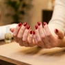 Woman's hands fanned on salon table showing ten freshly finished round nails in classic glossy red gel, warm lighting
