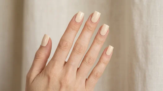 Woman's hand with short square nails in warm cream polish, fingers fanned showing crisp flat tip edges in studio lighting
