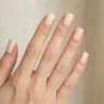 Woman's hand with short square nails in warm cream polish, fingers fanned showing crisp flat tip edges in studio lighting