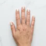 Overhead shot of hand on white marble surface showing soft cream marble nail design with delicate grey veining in daylight