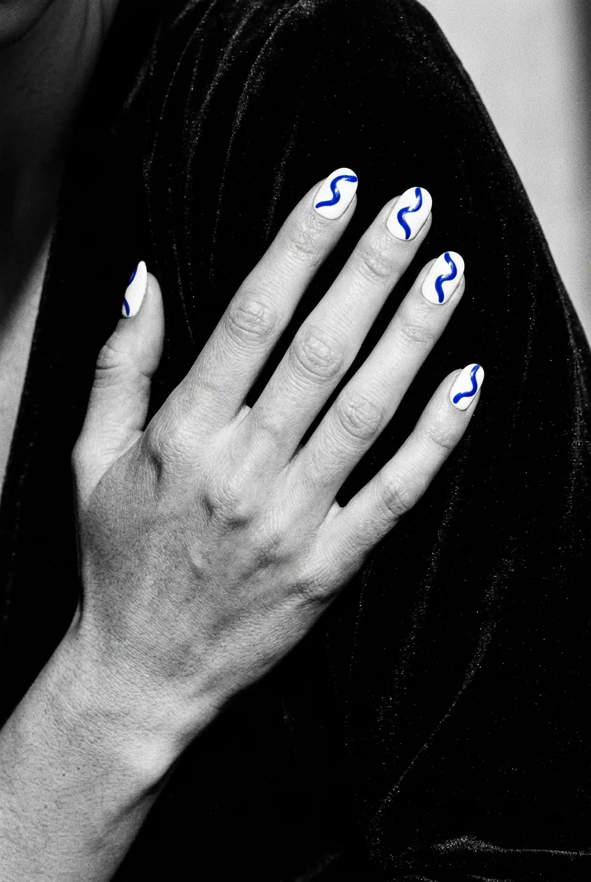 Manicured nails with clean white base and confident cobalt blue squiggle line drawn across each nail catching a sharp highlight under side light