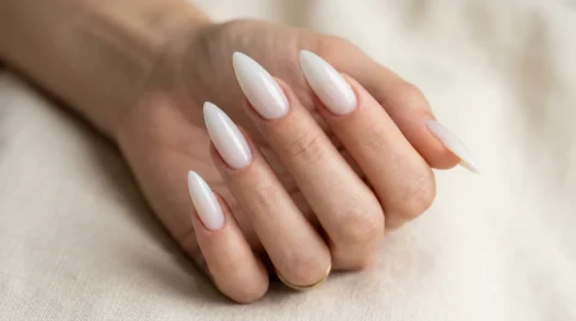 Woman's hand fanned out showing five long stiletto nails in a sheer glazed milky white finish against cream background