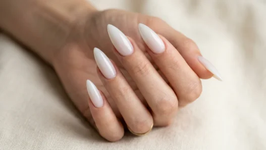 Woman's hand fanned out showing five long stiletto nails in a sheer glazed milky white finish against cream background