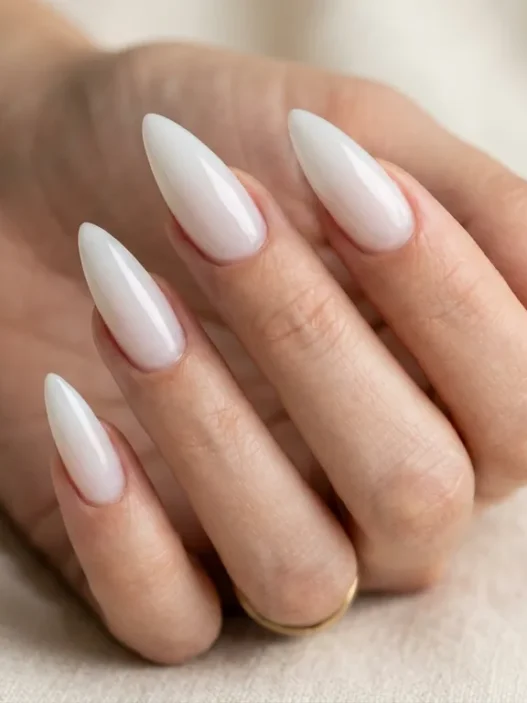 Woman's hand fanned out showing five long stiletto nails in a sheer glazed milky white finish against cream background