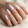 Woman's hand fanned out showing five long stiletto nails in a sheer glazed milky white finish against cream background