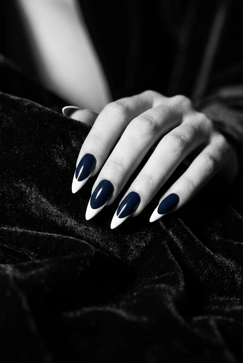 Manicured hand with stiletto nails in a two-tone French tip with deep midnight blue base and crisp white tip against dark velvet