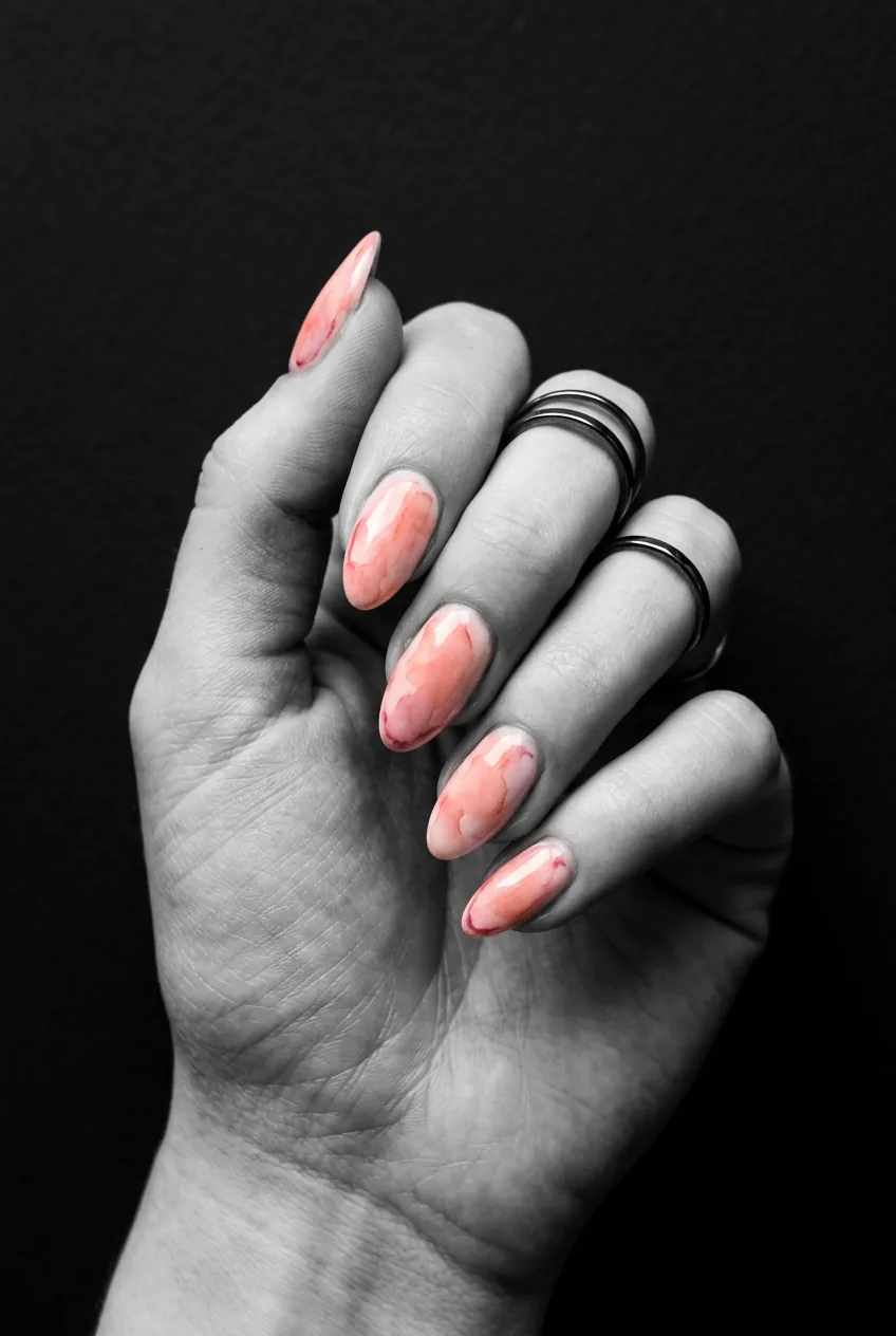 Close-up of nails with a loose watercolor wash in translucent coral and blush pink with defined darker edges under soft dramatic lighting